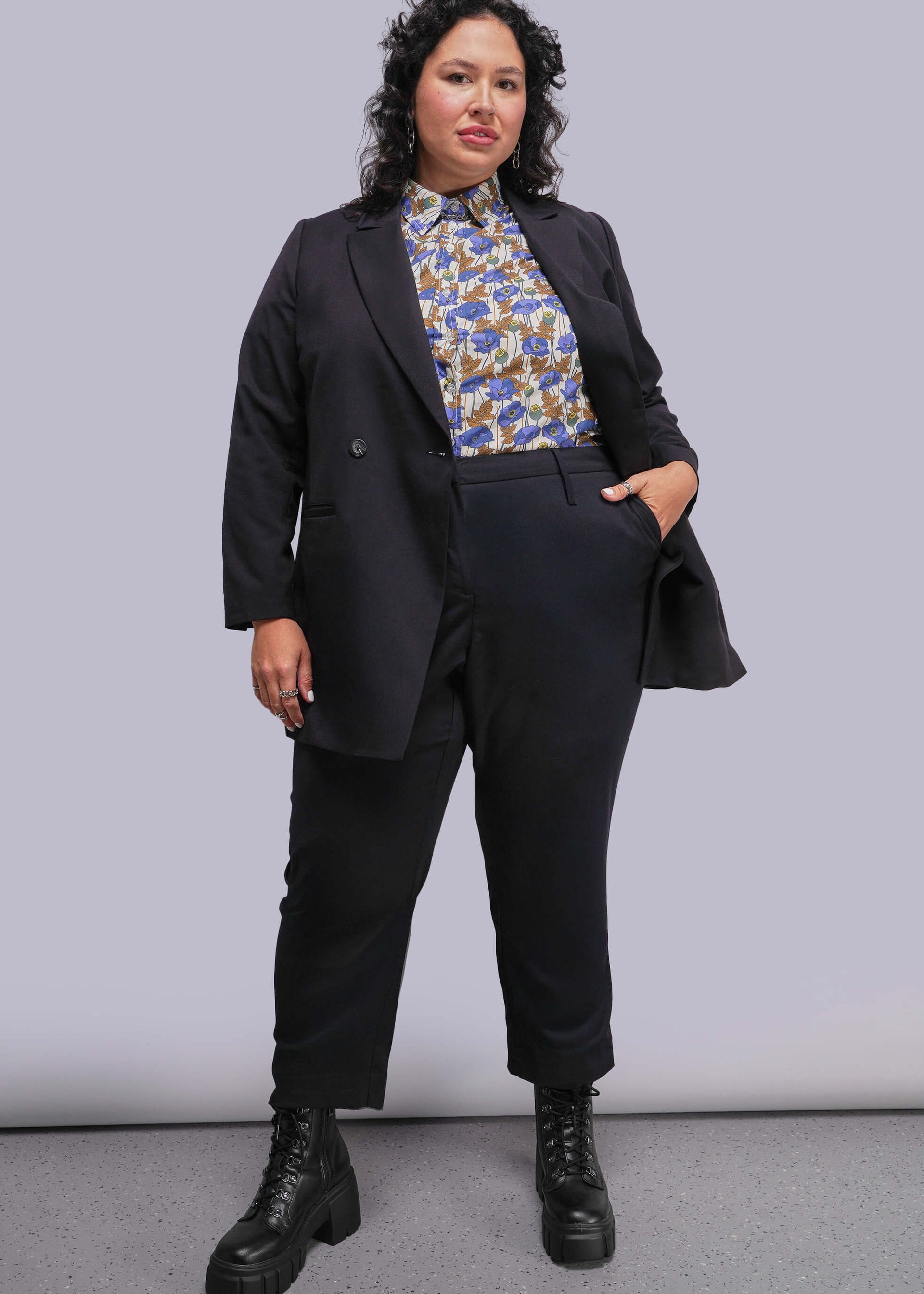 1X=Person wearing a black suit with a floral blouse against a plain background