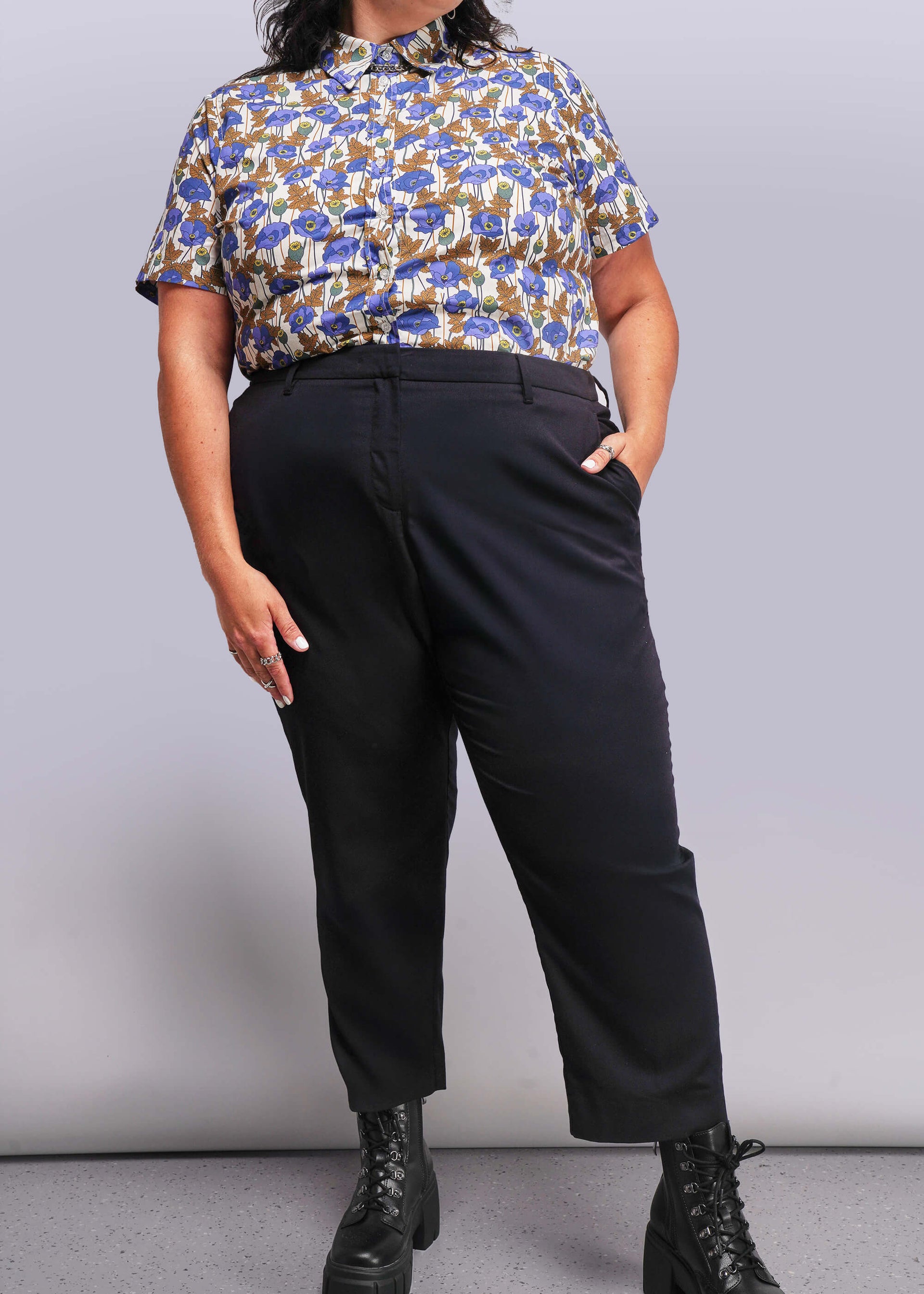 1X=Person wearing a floral blouse and black pants against a plain background