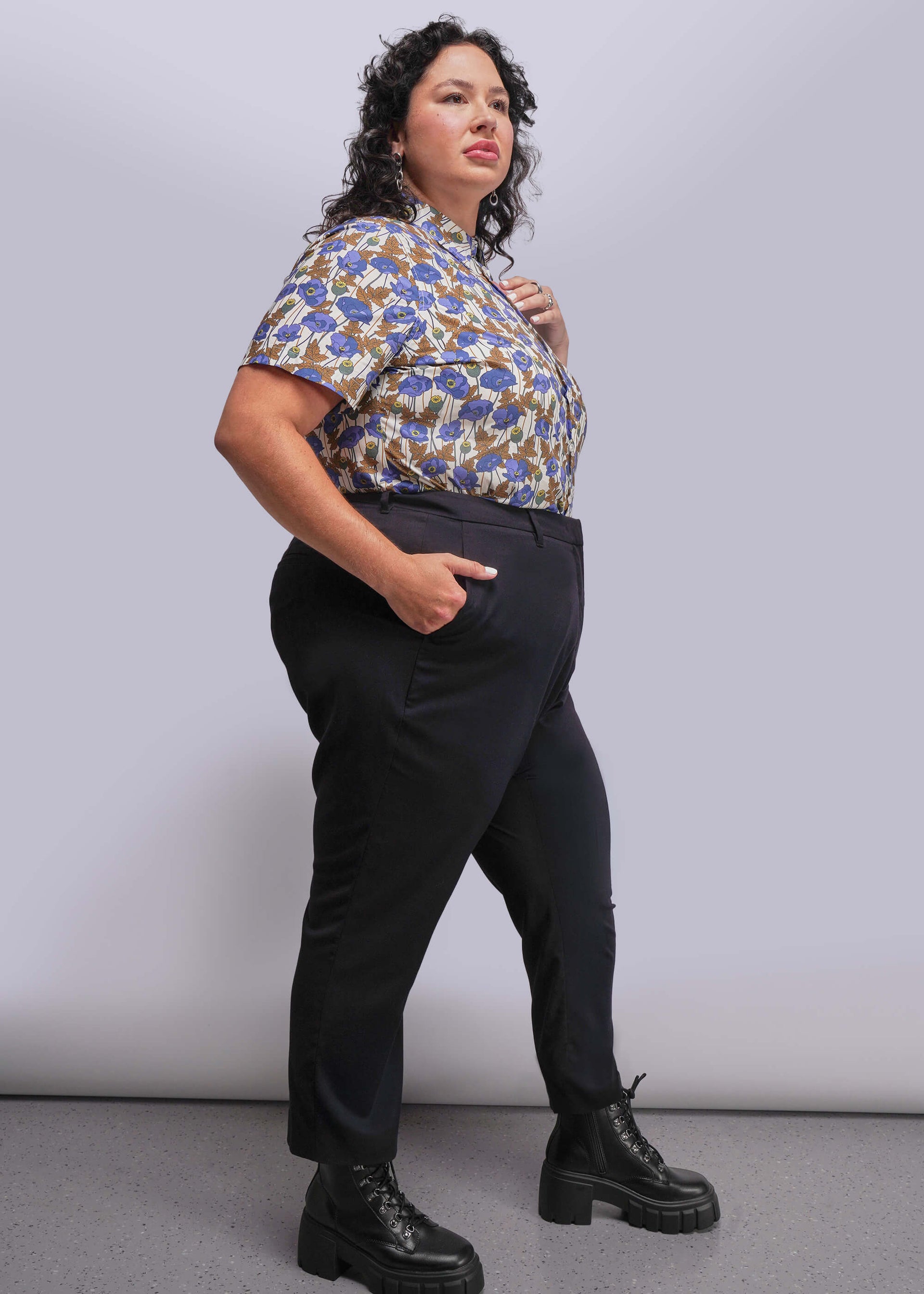 1X=Person wearing a floral blouse and black pants against a plain background