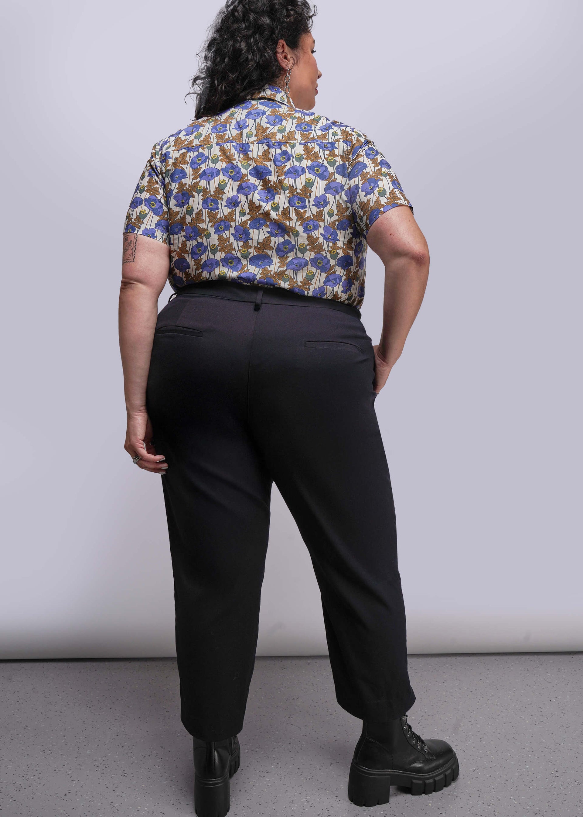 1X=Person wearing a patterned shirt and black pants against a plain background
