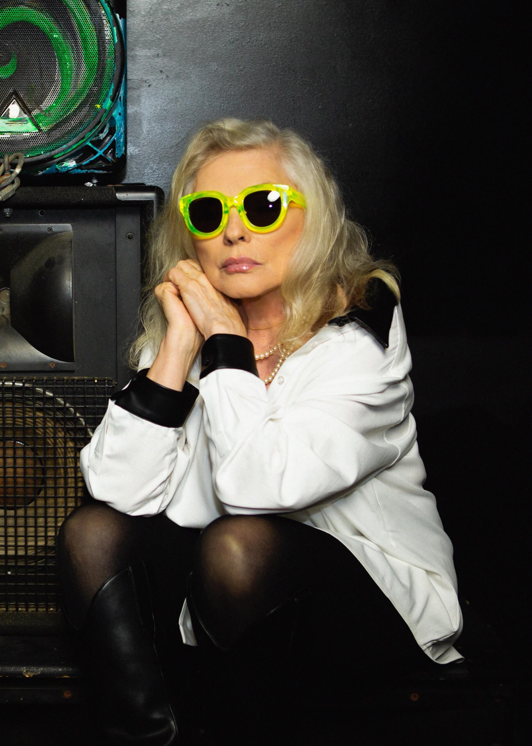 Person wearing yellow sunglasses sitting in a dark room with electronic equipment.
