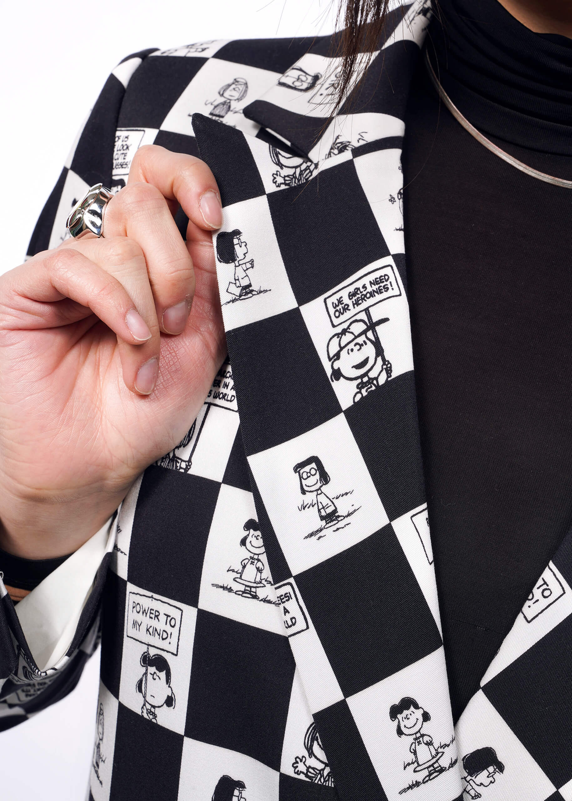S=Close up of model holding the lapel of The Peanuts x Wildfang Double Breasted Blazer in a custom black and white checkered print featuring Peanuts characters.