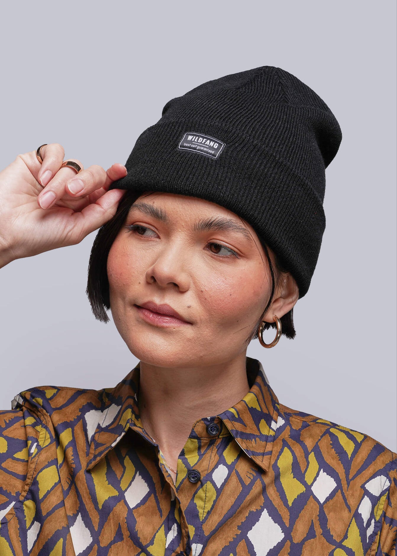 Person wearing a black beanie and a patterned shirt against a plain background