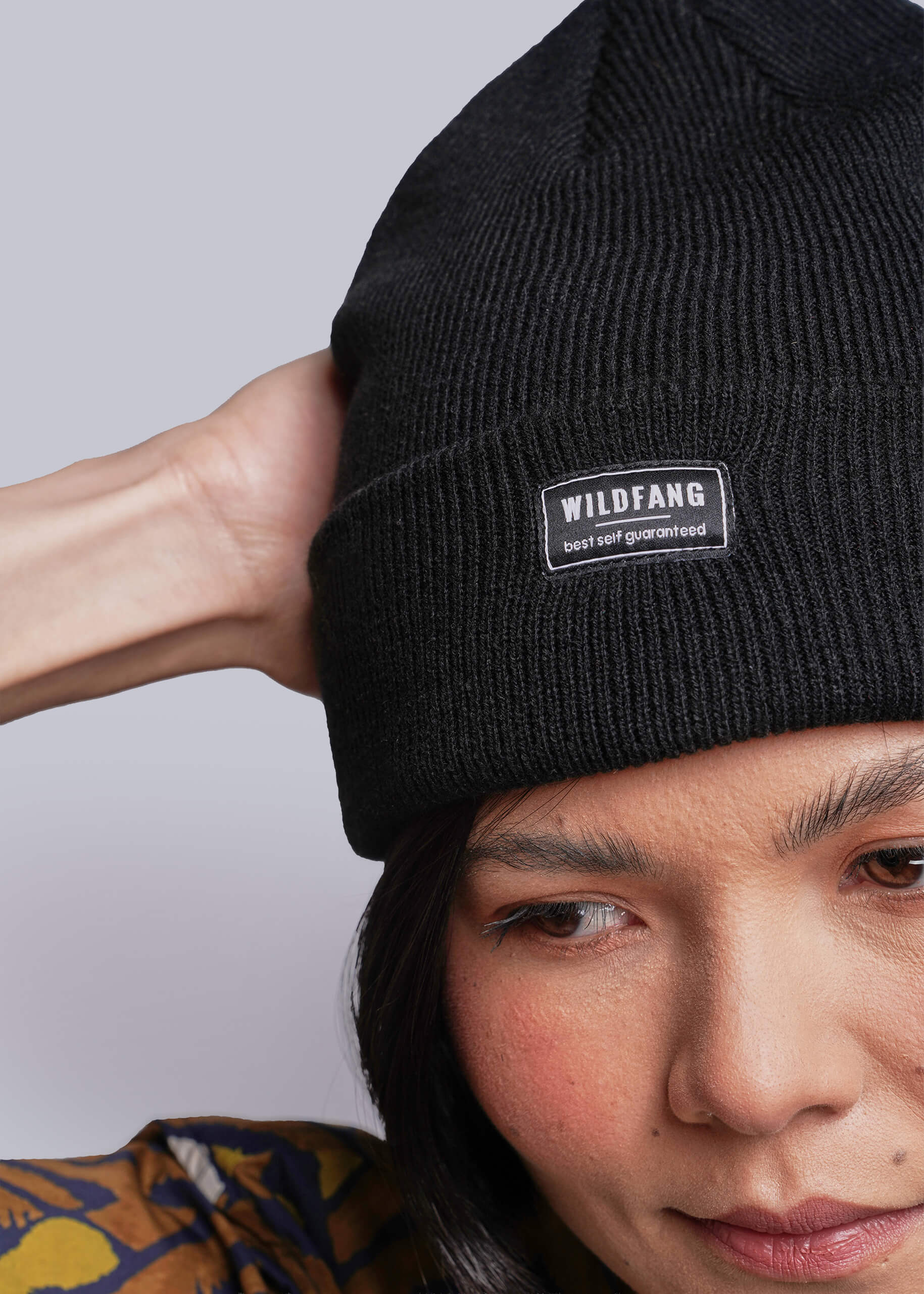 Person wearing a black beanie with a 'WILDFANG' label against a light purple background