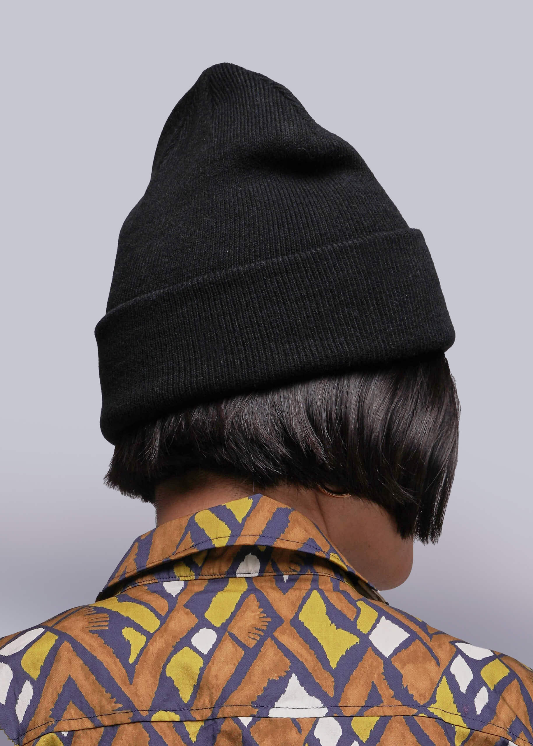 Person wearing a black beanie and patterned shirt on a gray background