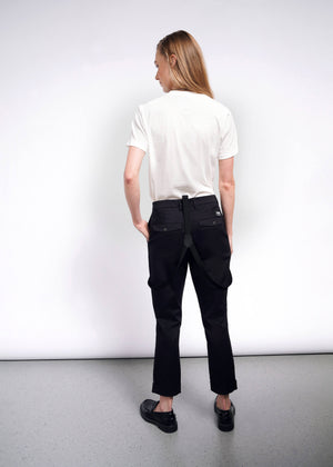 S=A person with long hair, facing away, stands against a white background. Theyre wearing a Debbie Harry X Wildfang Graphic Tee, black pants with hanging suspenders, and black shoes, embodying punk fashion effortlessly.