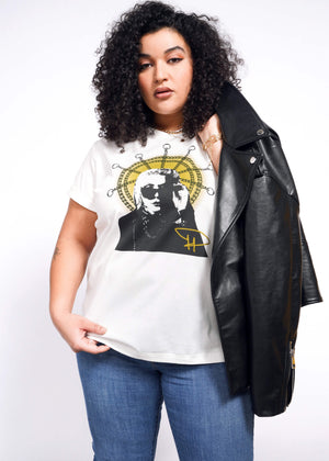 1X= With curly hair, a person sports a Debbie Harry X Wildfang Graphic Tee featuring an abstract design while slinging a black leather jacket over one shoulder, exuding punk fashion against a plain white backdrop.