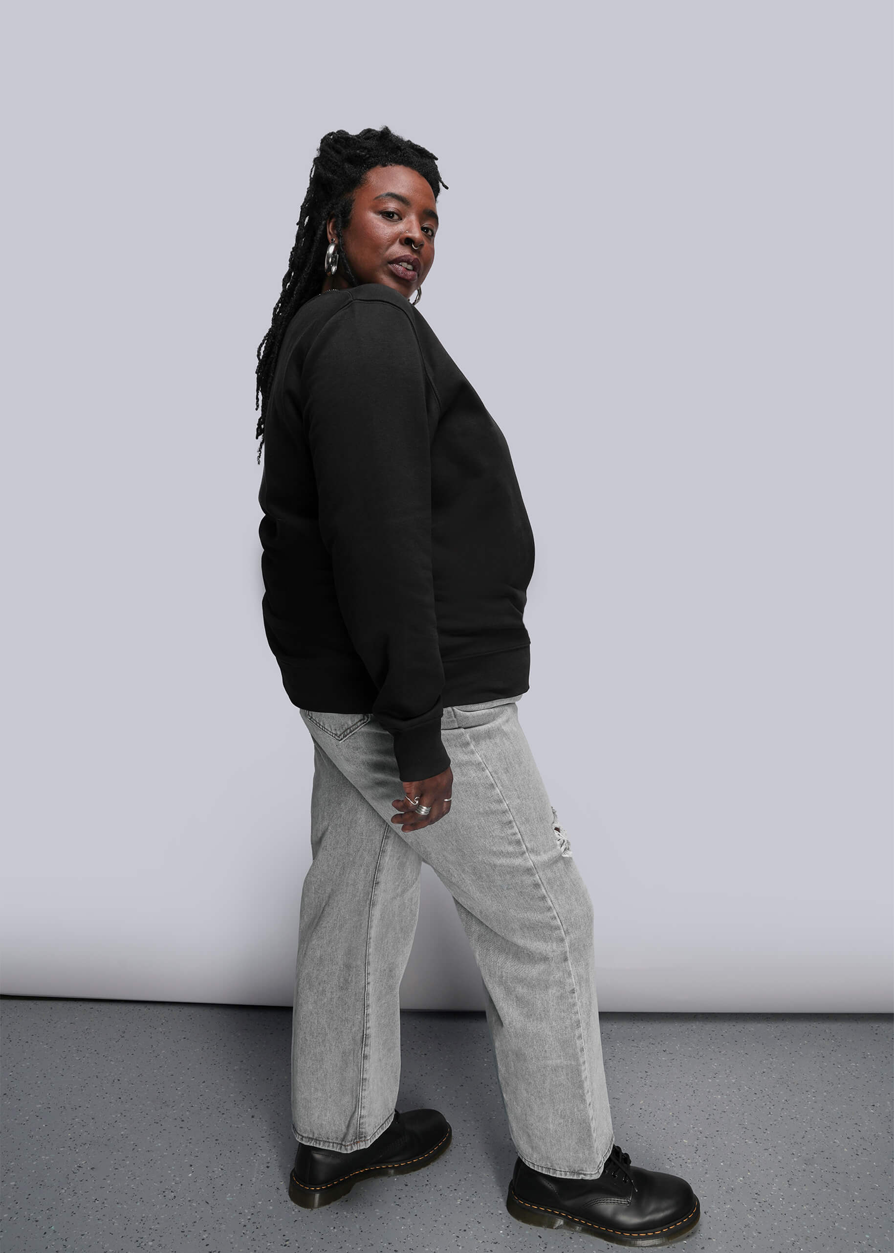 1X=Person wearing a black crew neck and light gray pants against a white background