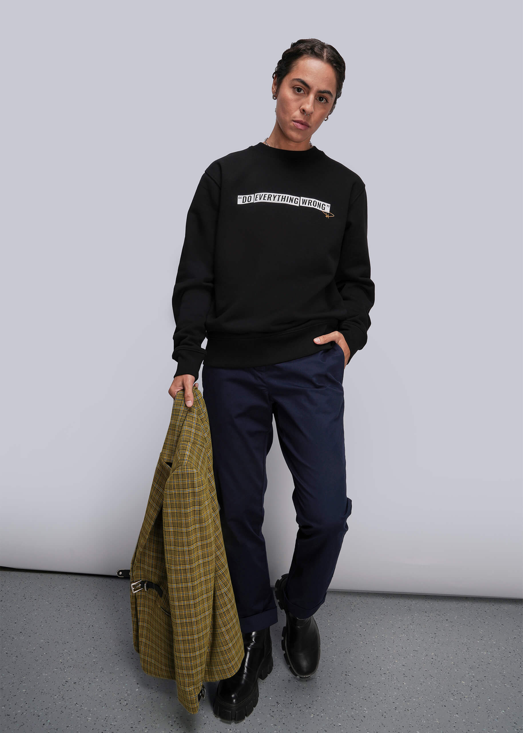 S=Person wearing a black sweatshirt with text, holding a green coat against a plain background