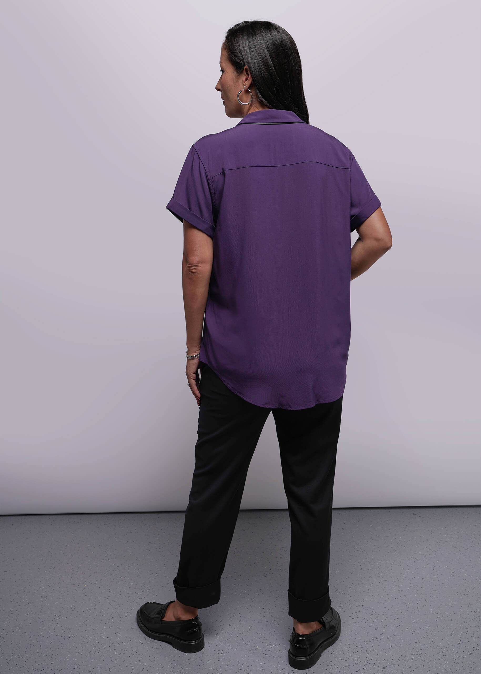 S=Person wearing a purple shirt and black pants against a plain background