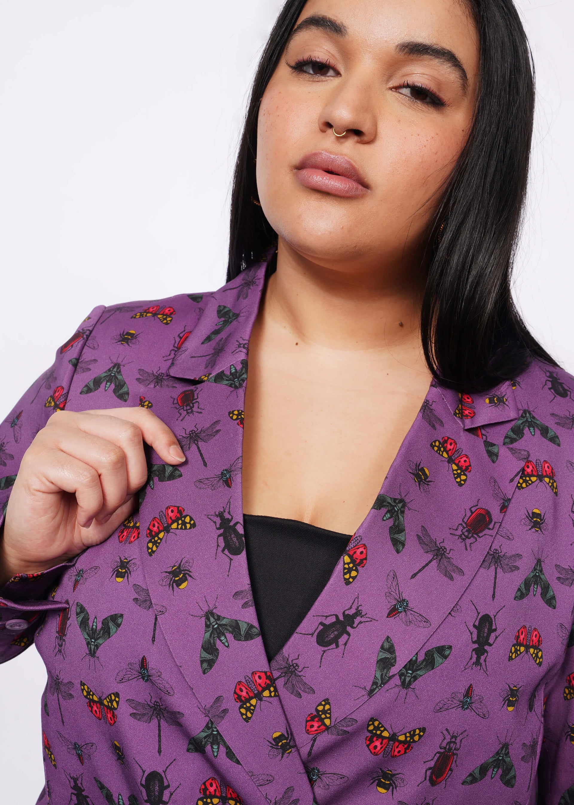 1X= Close up of person with long black hair holding lapel of purple bug printed blazer