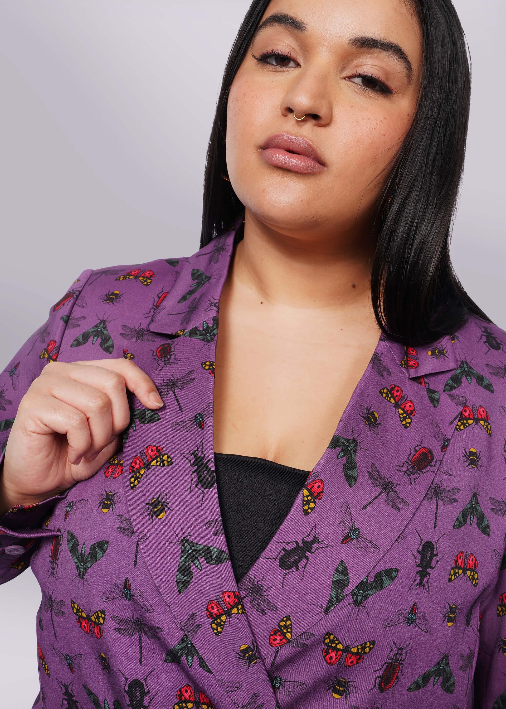 1X= Close up of person with long black hair holding lapel of purple bug printed blazer