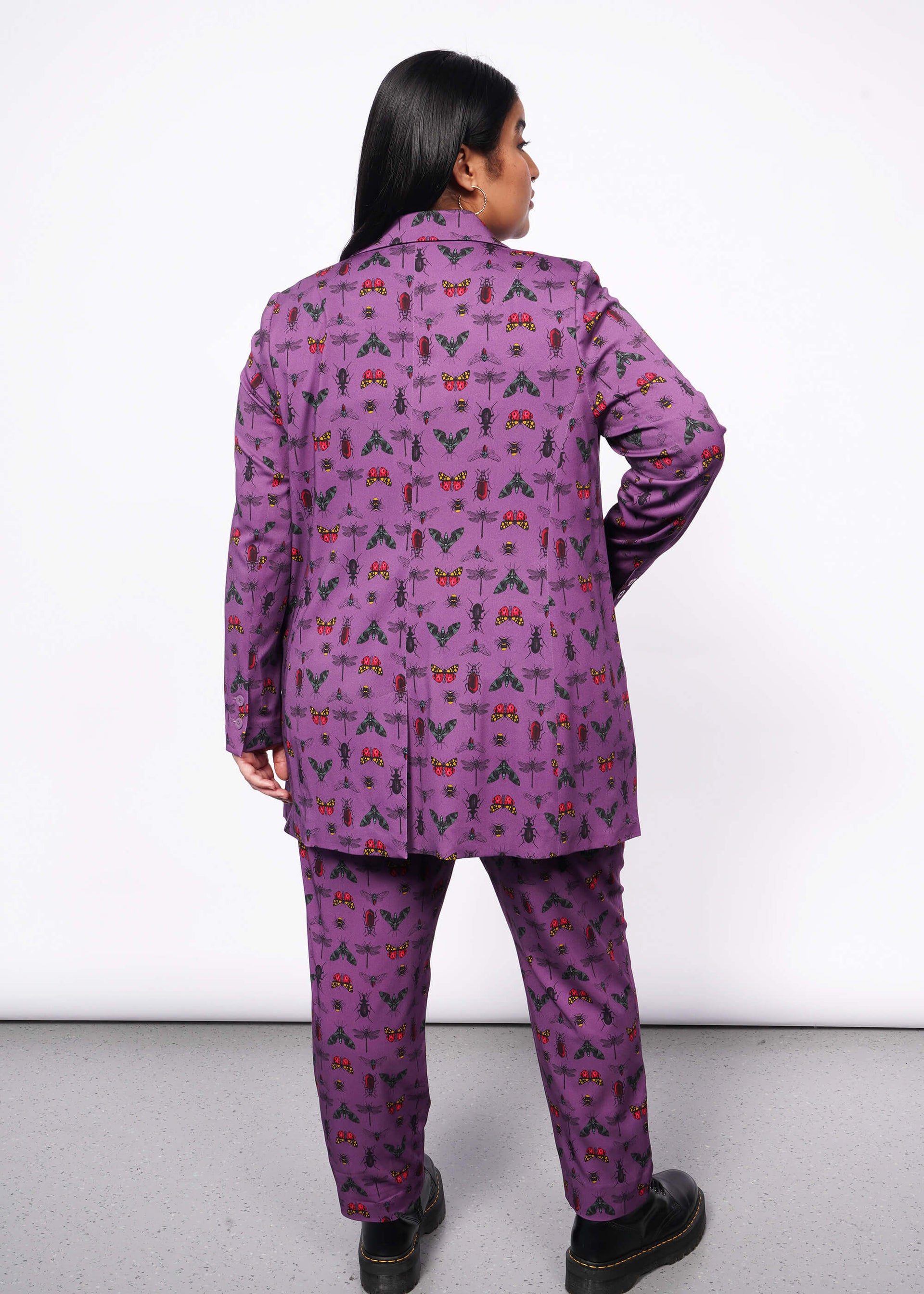 1X=Back view of person with long black hair with hand in double breasted blazer pocket. Is wearing matching trouser and black boots.