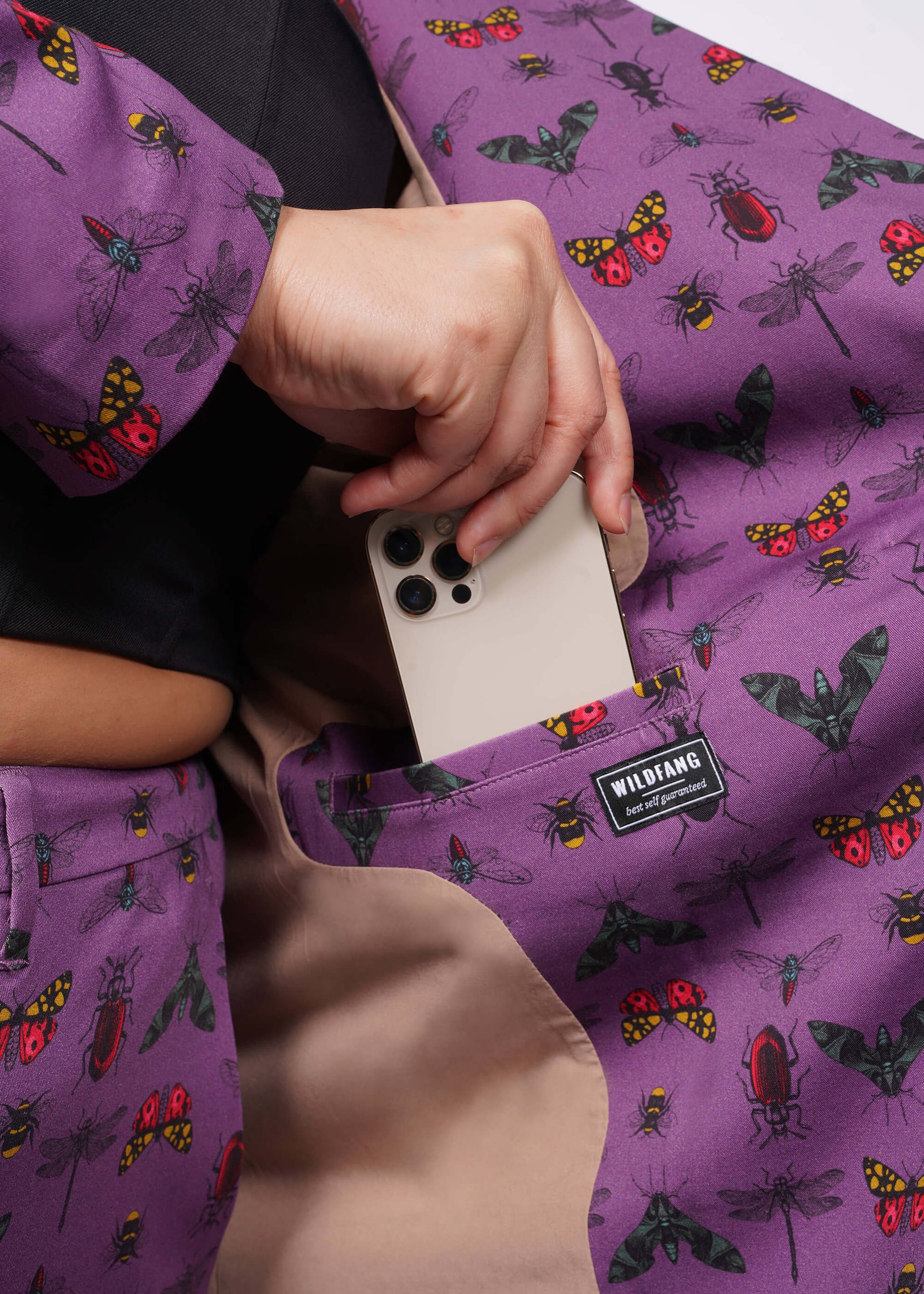 1X=Close up of inside of purple bug printed blazer showing model putting iphone into interior pocket.