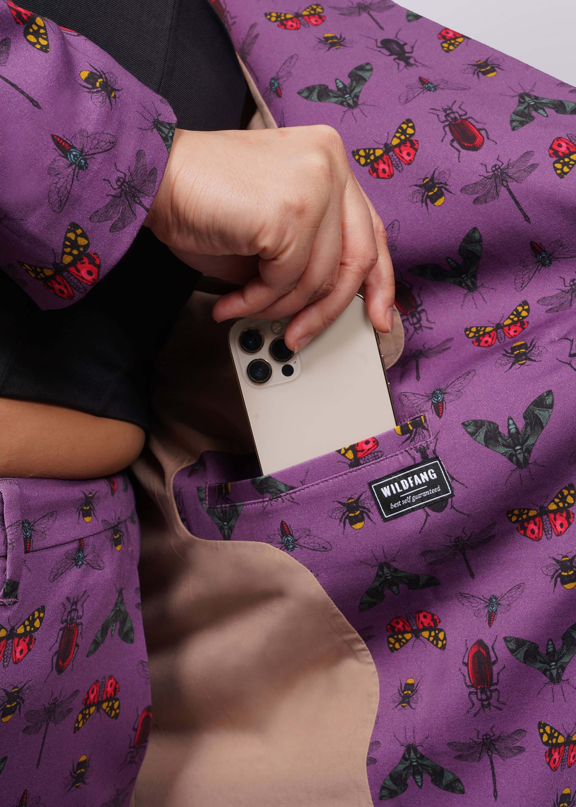 1X=Close up of inside of purple bug printed blazer showing model putting iphone into interior pocket.
