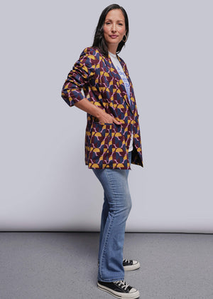 S=Woman wearing a colorful patterned jacket and blue jeans against a plain background