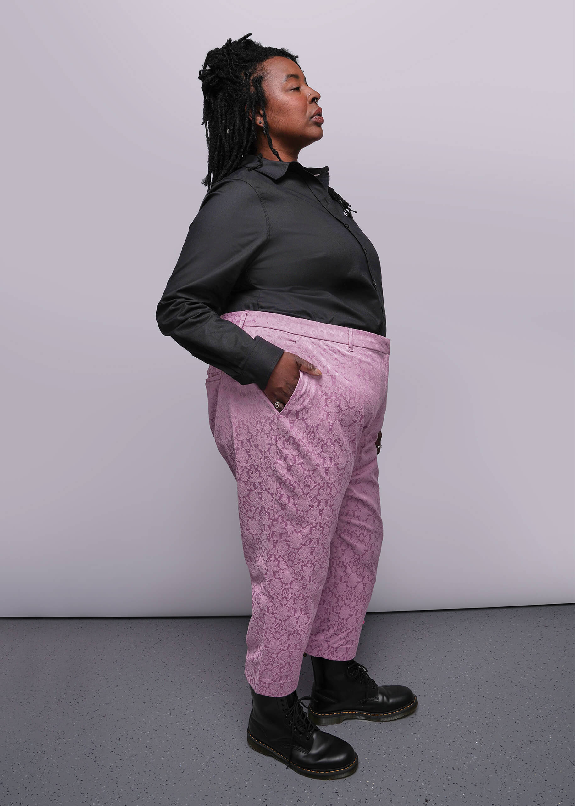 1X=Person wearing a black long-sleeve top and pink patterned pants against a plain background