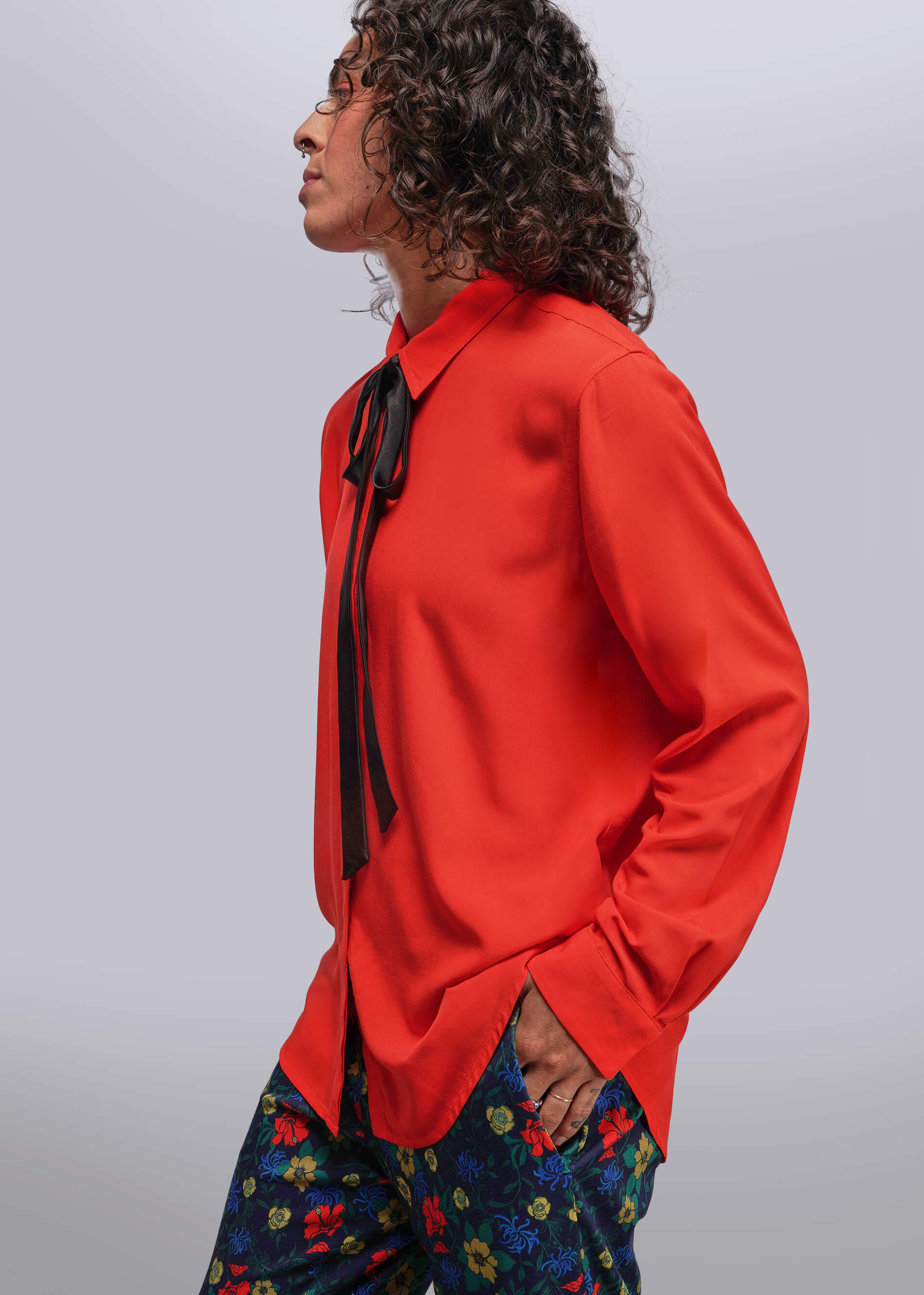 S=Person wearing a bright red shirt with a black tie and colorful pants on a light gray background