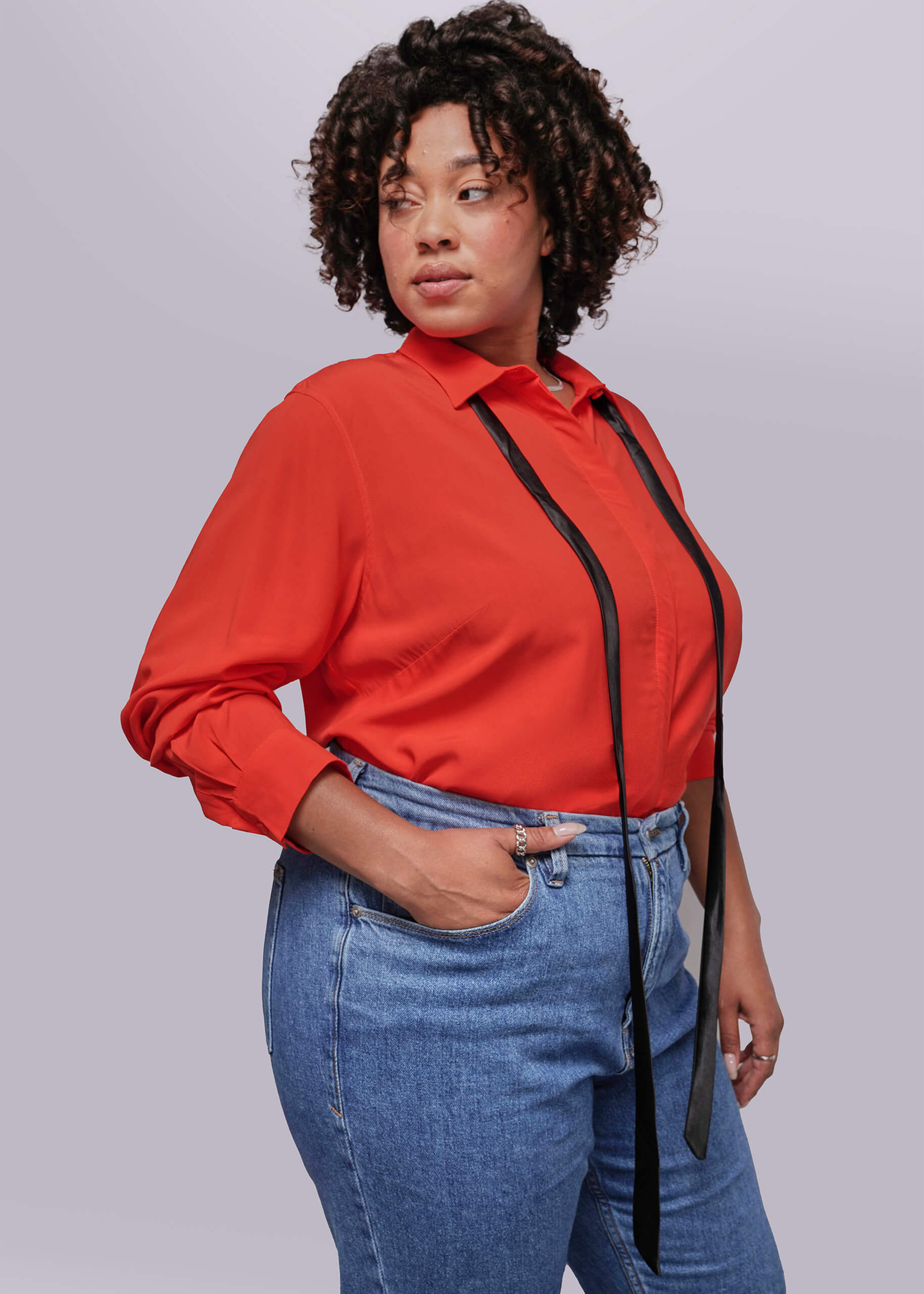 1X=Person wearing a red blouse with a black ribbon and blue jeans on a plain background