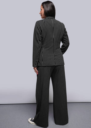 S=Person wearing a black and white pinstripe suit standing against a plain background