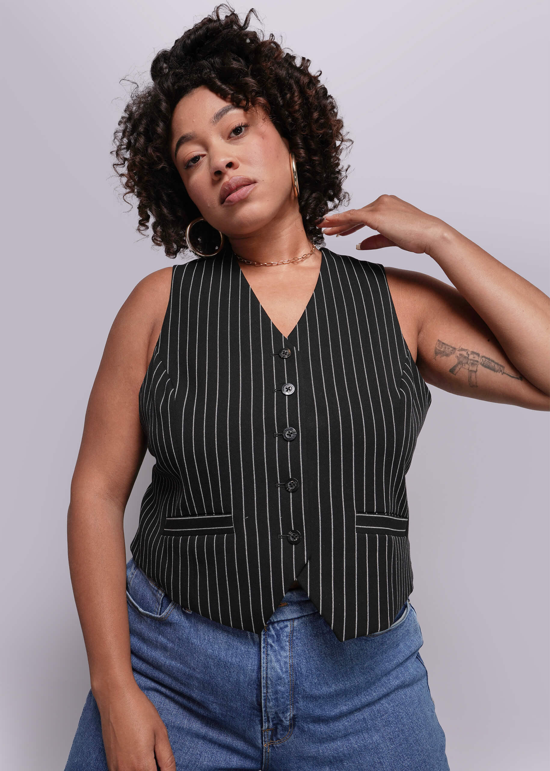 1X=Woman wearing a black pinstripe vest over a blue top against a plain background