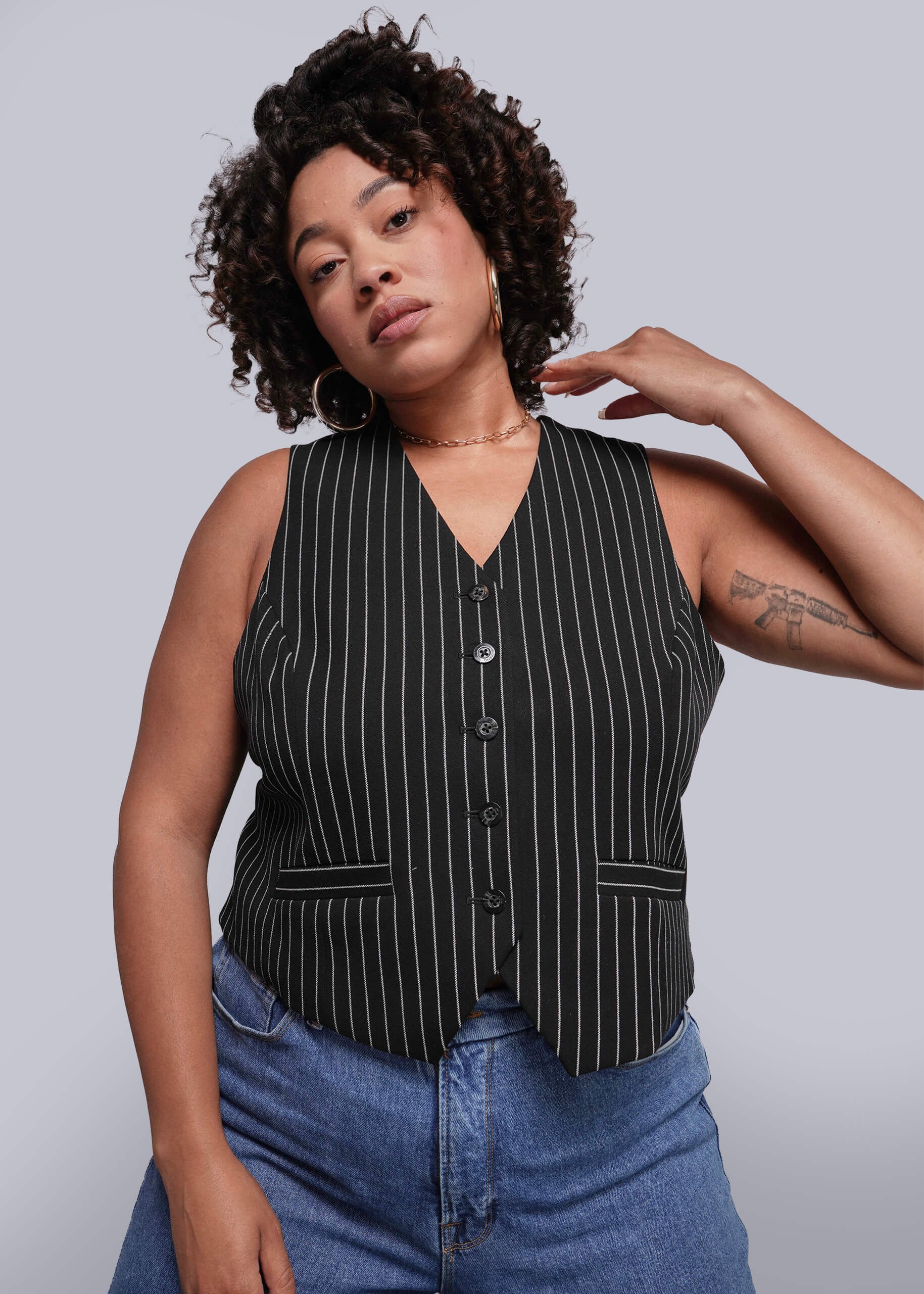 1X=Woman wearing a black pinstripe vest over a blue top against a plain background