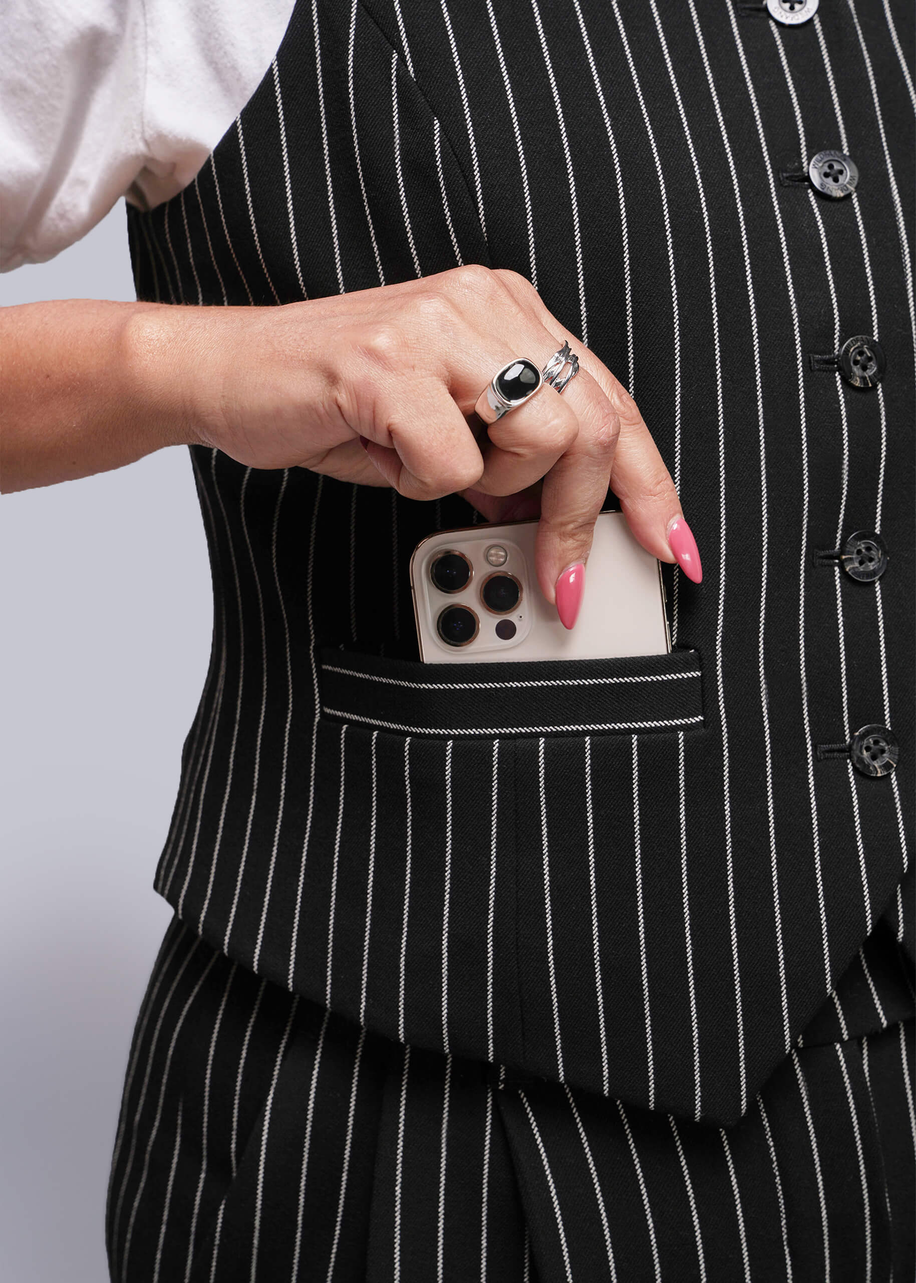 S=Person wearing a black pinstripe suit with a phone in the pocket against a neutral background