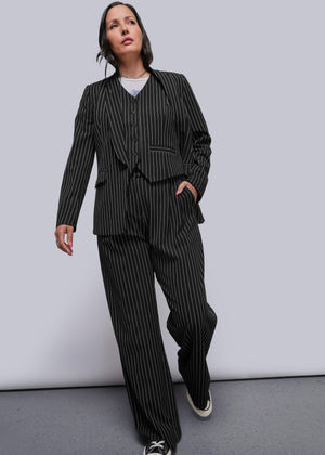 1X=Person wearing a black pinstripe suit with sneakers on a plain background