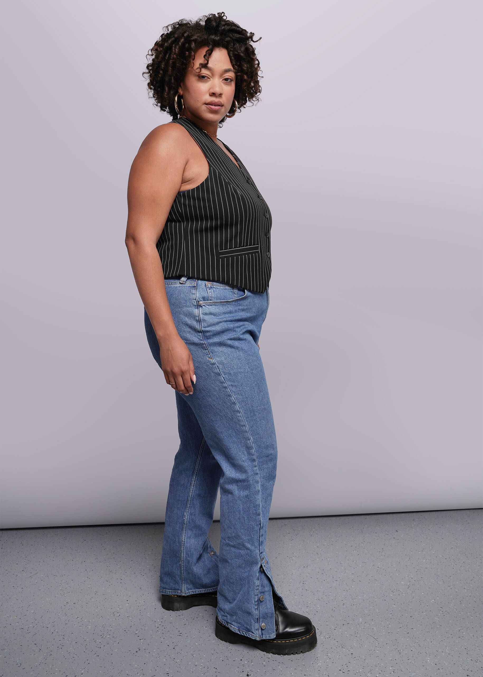 1X=Woman wearing a black sleeveless top and blue jeans against a plain background