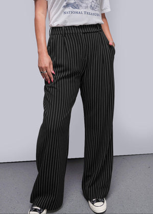 S=Person wearing a graphic t-shirt and pinstripe pants against a plain background