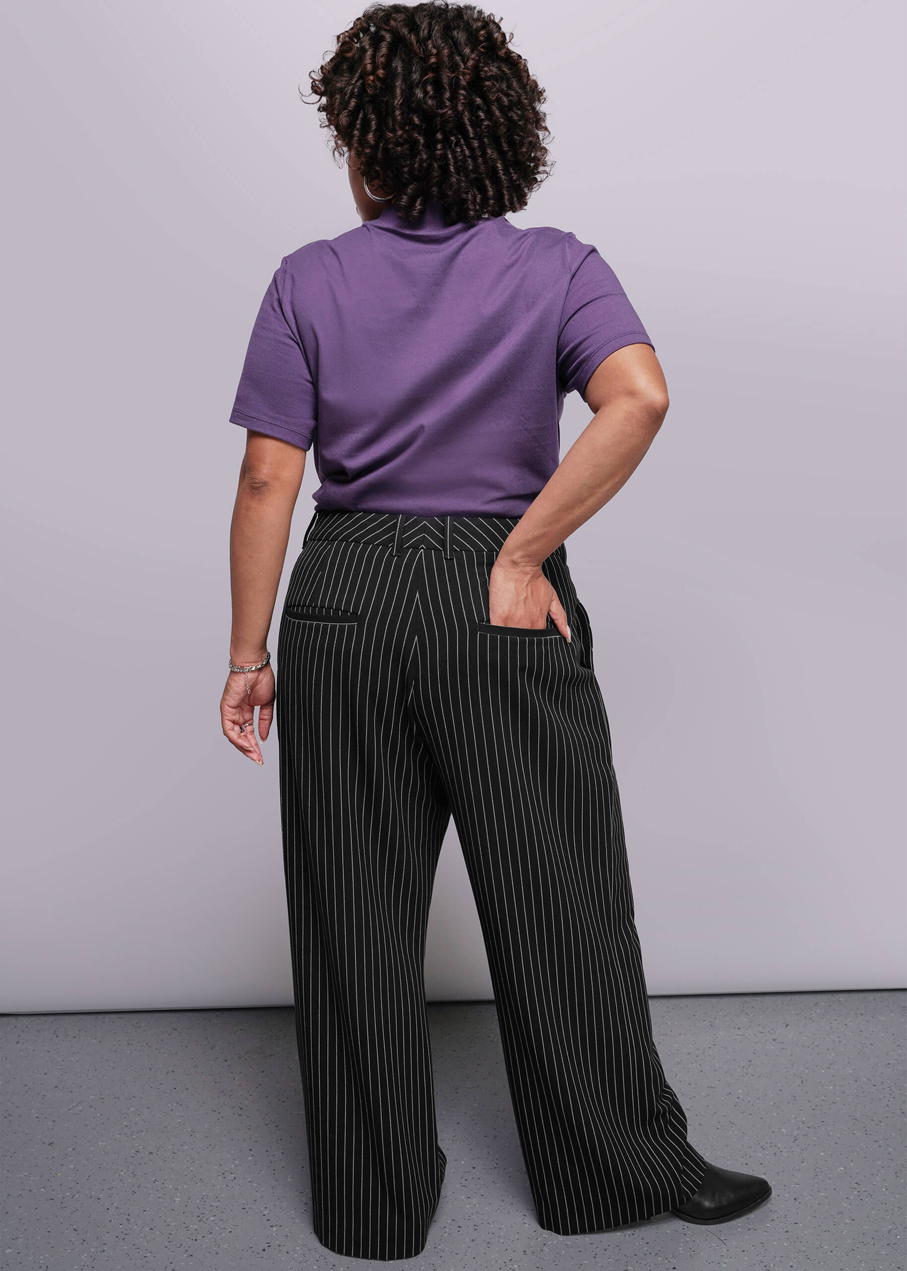 1X=Person wearing a purple shirt and black pinstripe pants against a gray background