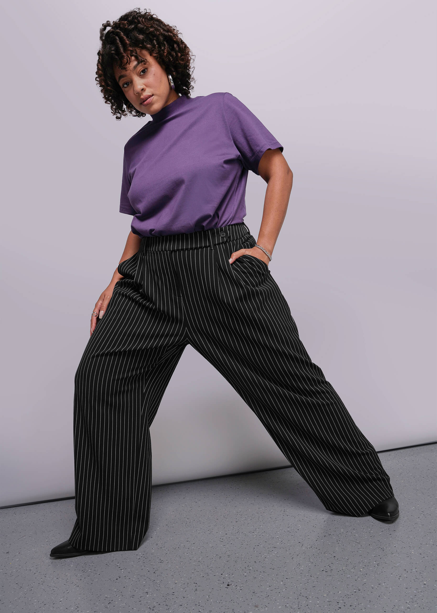 1X=Person wearing a purple shirt and black pinstripe pants against a gray background