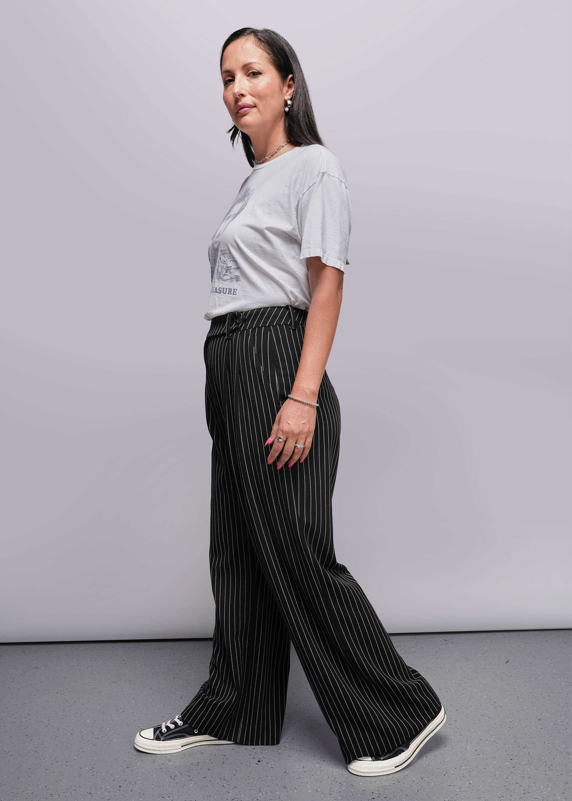 S=Woman wearing a white t-shirt and black pinstripe pants against a plain background