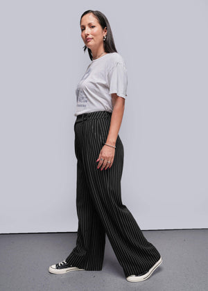S=Woman wearing a white t-shirt and black pinstripe pants against a plain background