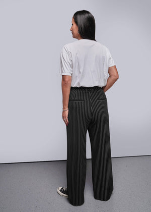 S=Person wearing a white shirt and black pinstripe pants against a plain background