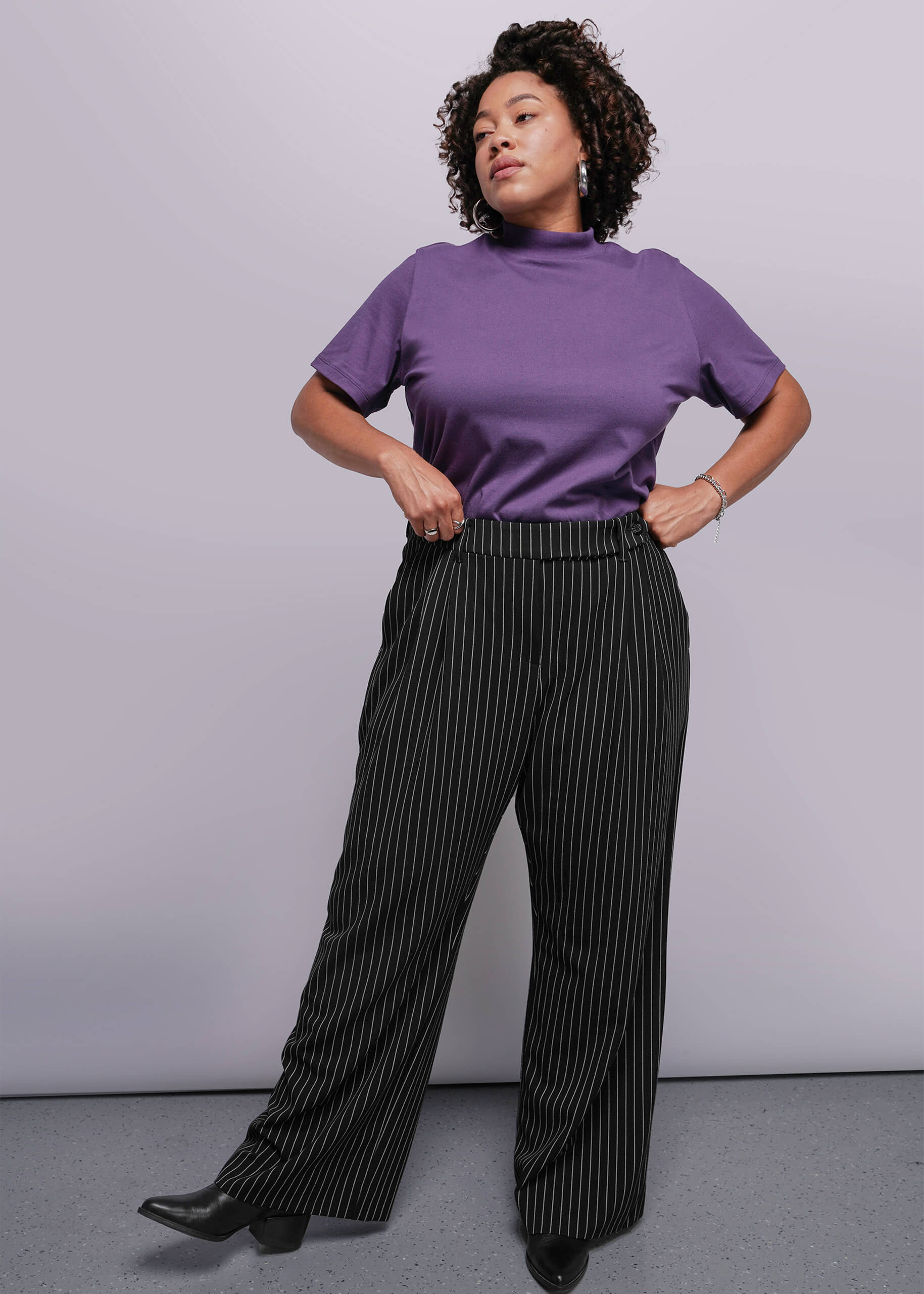 1X=Person wearing a purple top and black pinstripe pants against a plain background