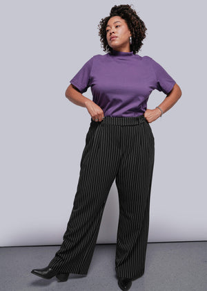 1X=Person wearing a purple top and black pinstripe pants against a plain background