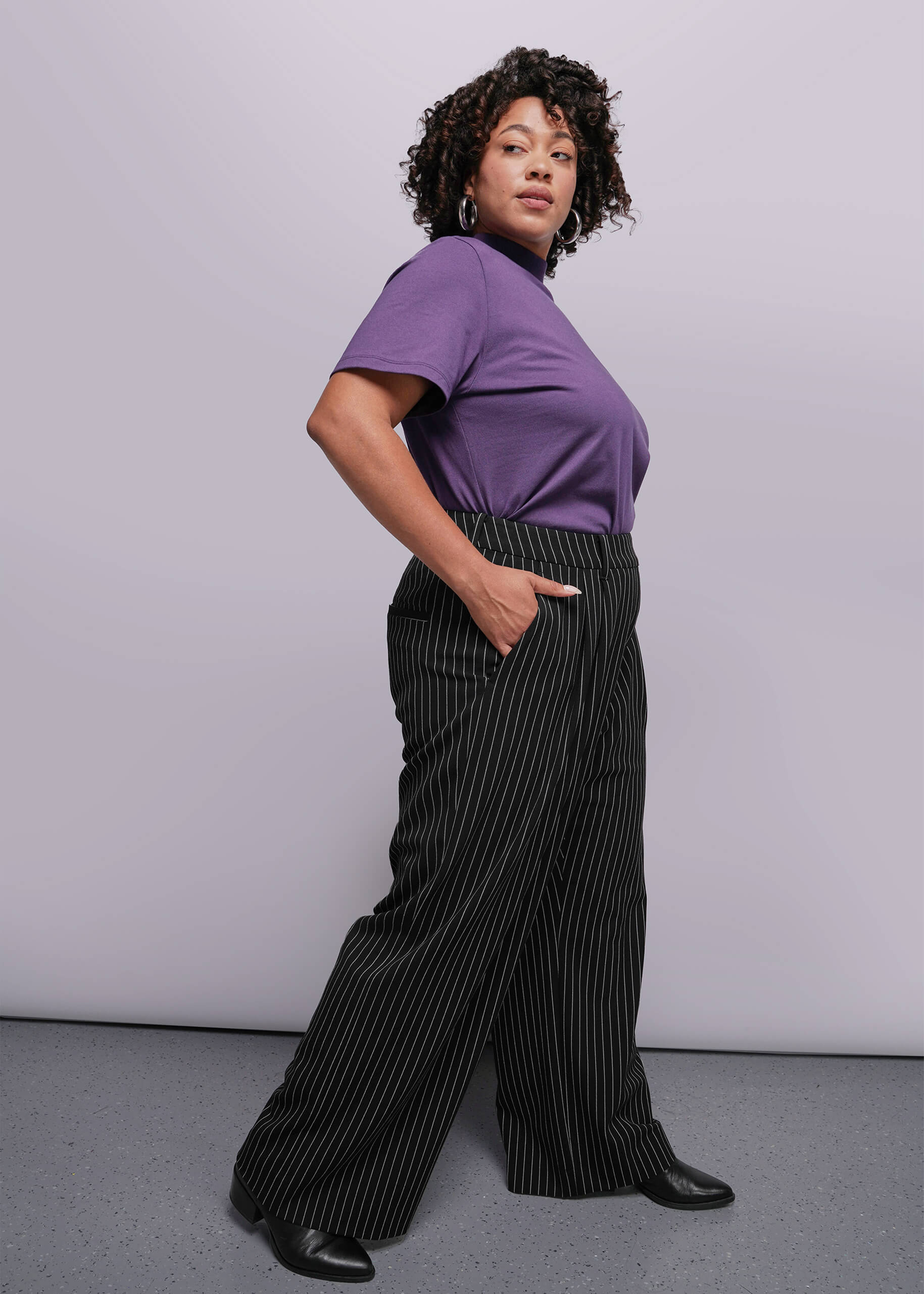 1X=Person wearing a purple top and black pinstripe pants against a plain background