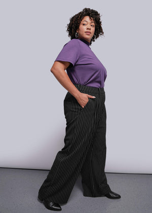 1X=Person wearing a purple top and black pinstripe pants against a plain background