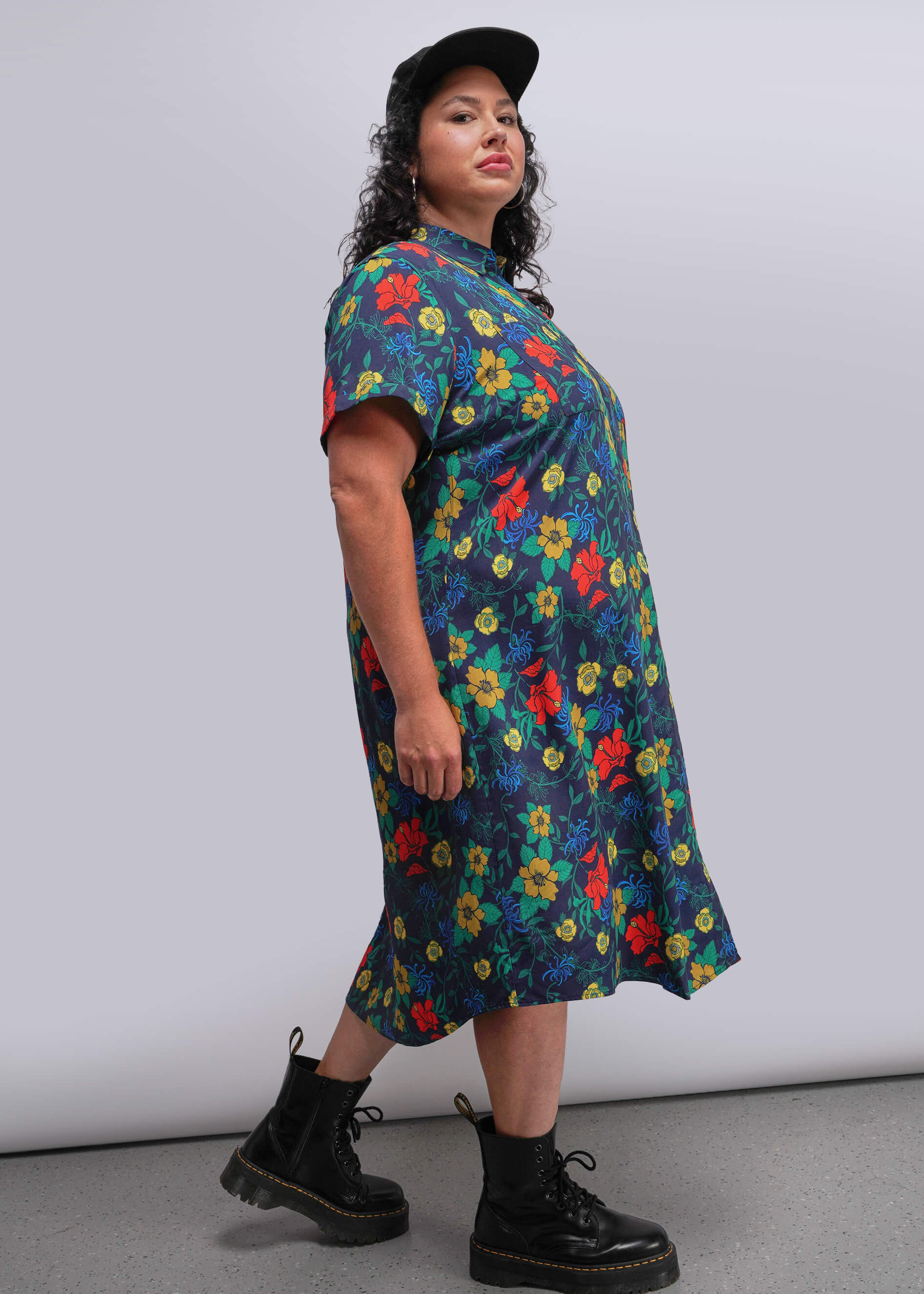 1X=Side view of person wearing a colorful floral dress with black boots against a plain background