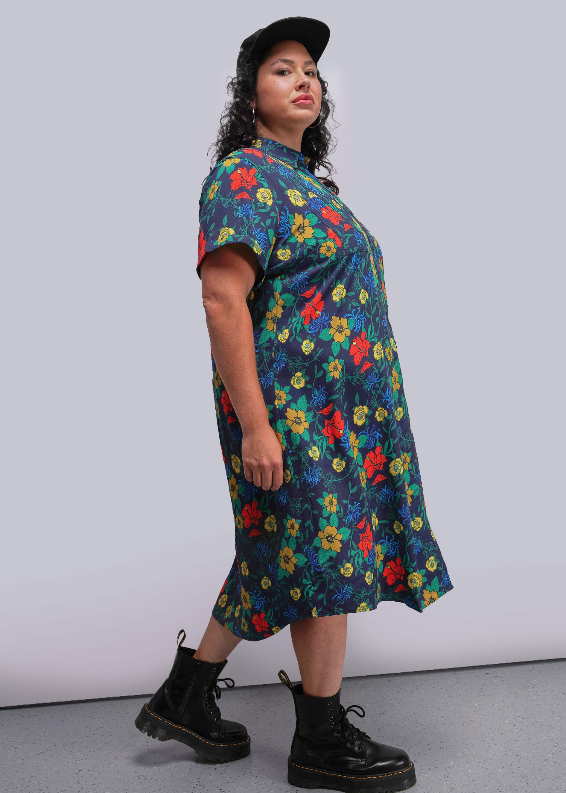 1X=Side view of person wearing a colorful floral dress with black boots against a plain background