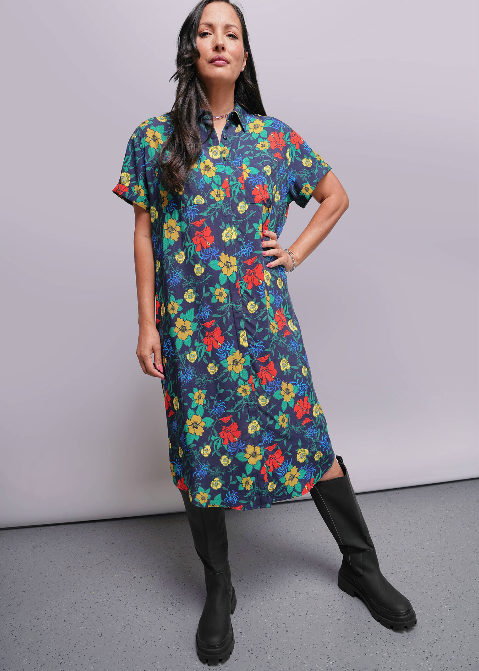 S=Woman wearing a colorful floral dress with black boots against a plain background