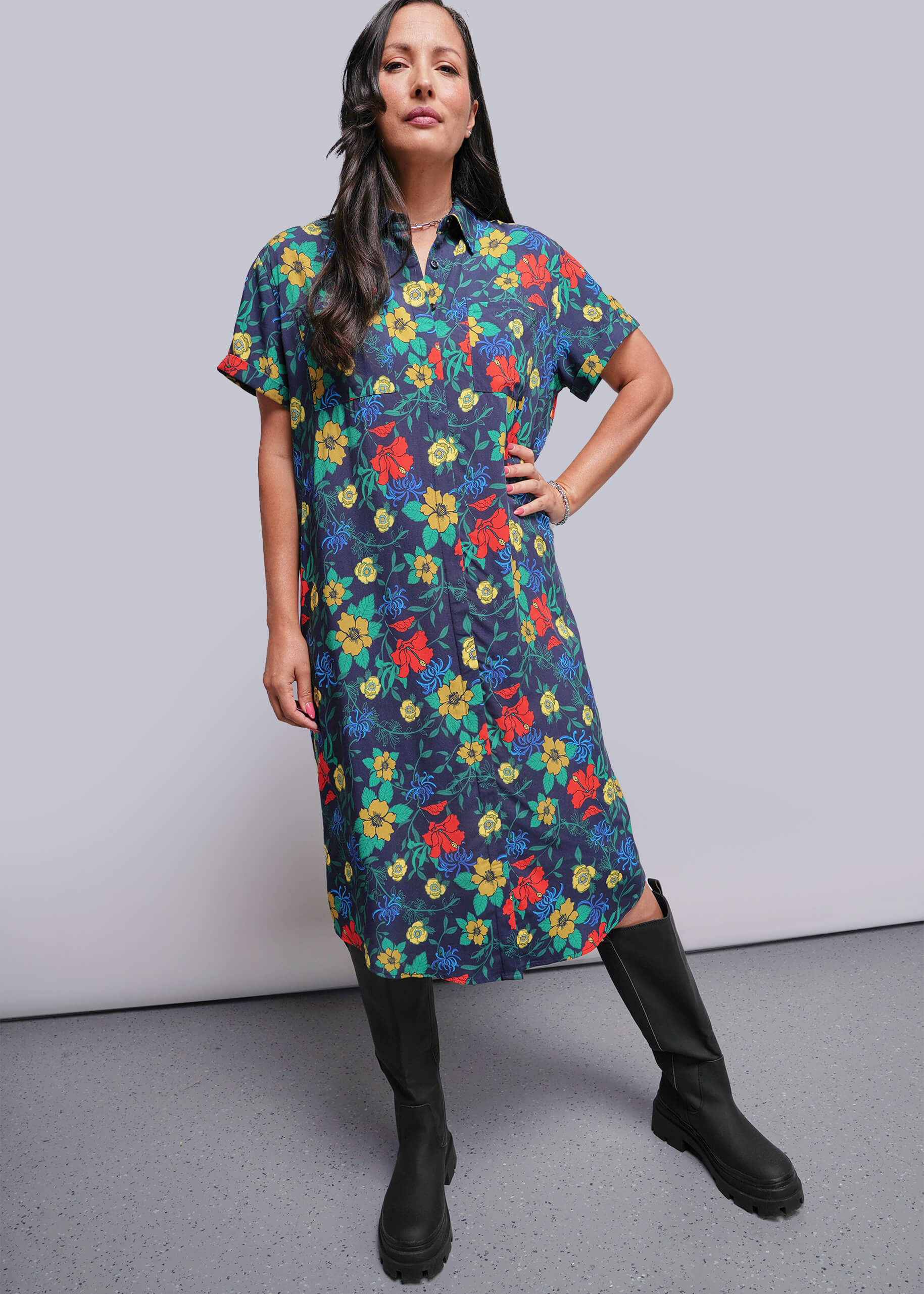 S=Woman wearing a colorful floral dress with black boots against a plain background