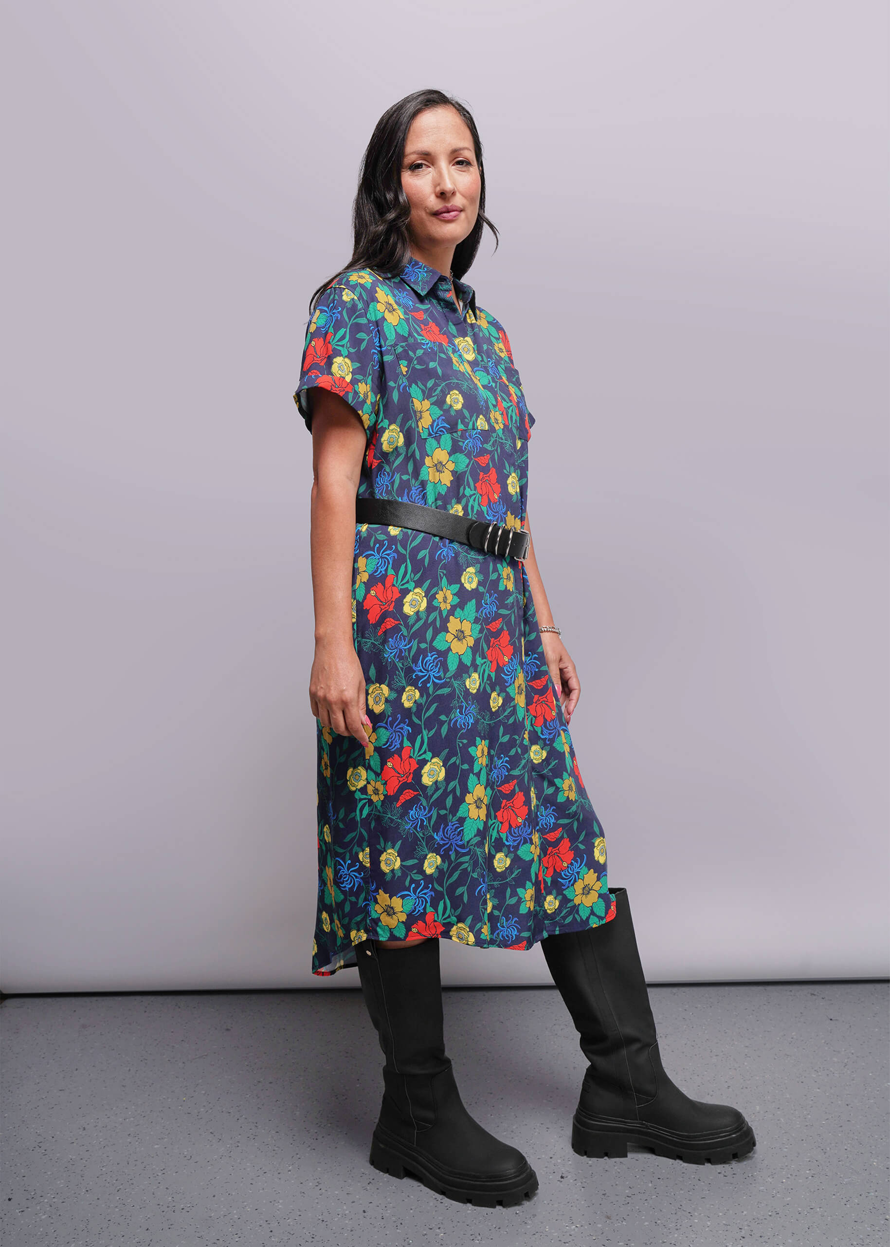 S=Woman wearing a colorful floral dress with black boots against a plain background