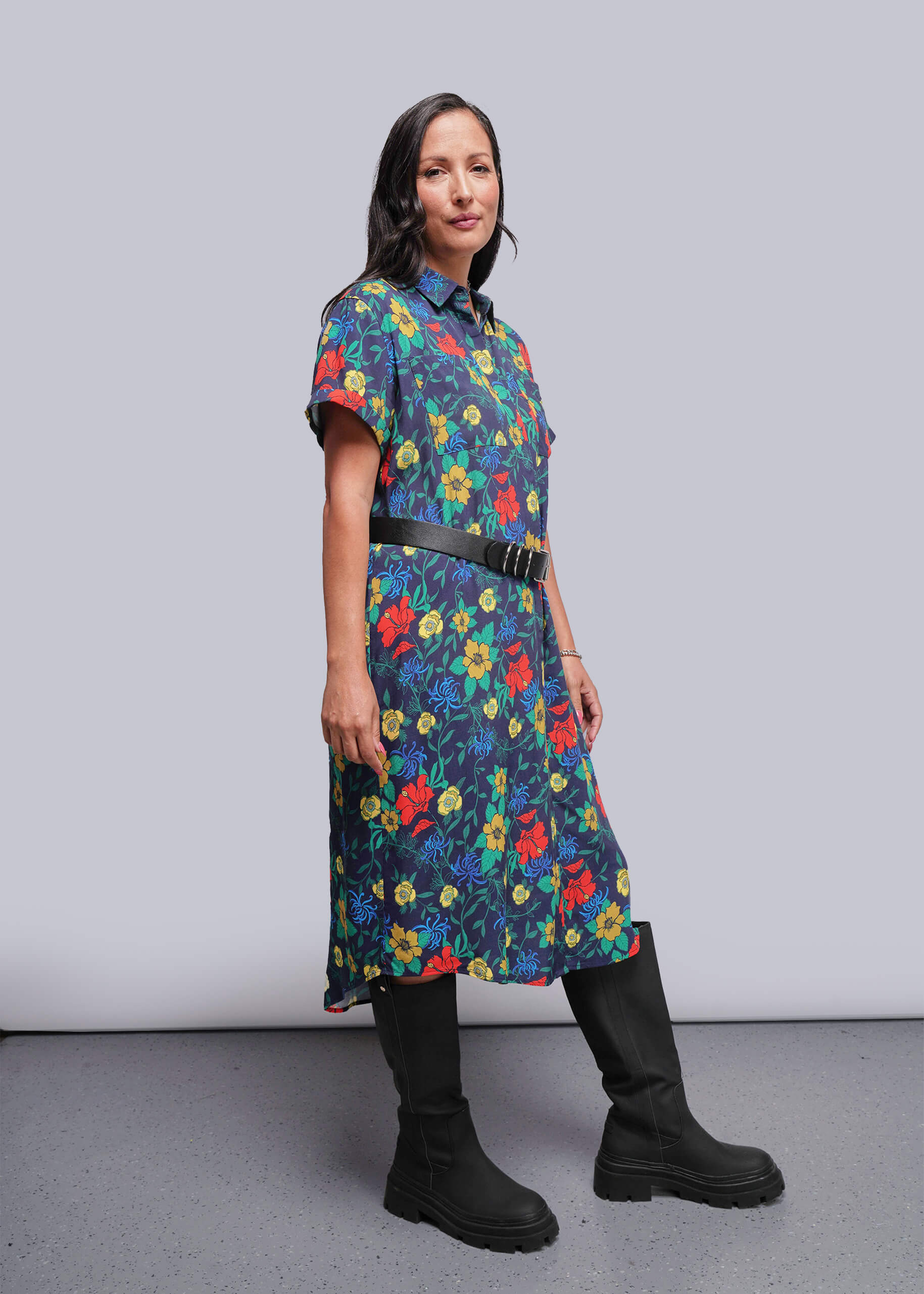 S=Woman wearing a colorful floral dress with black boots against a plain background