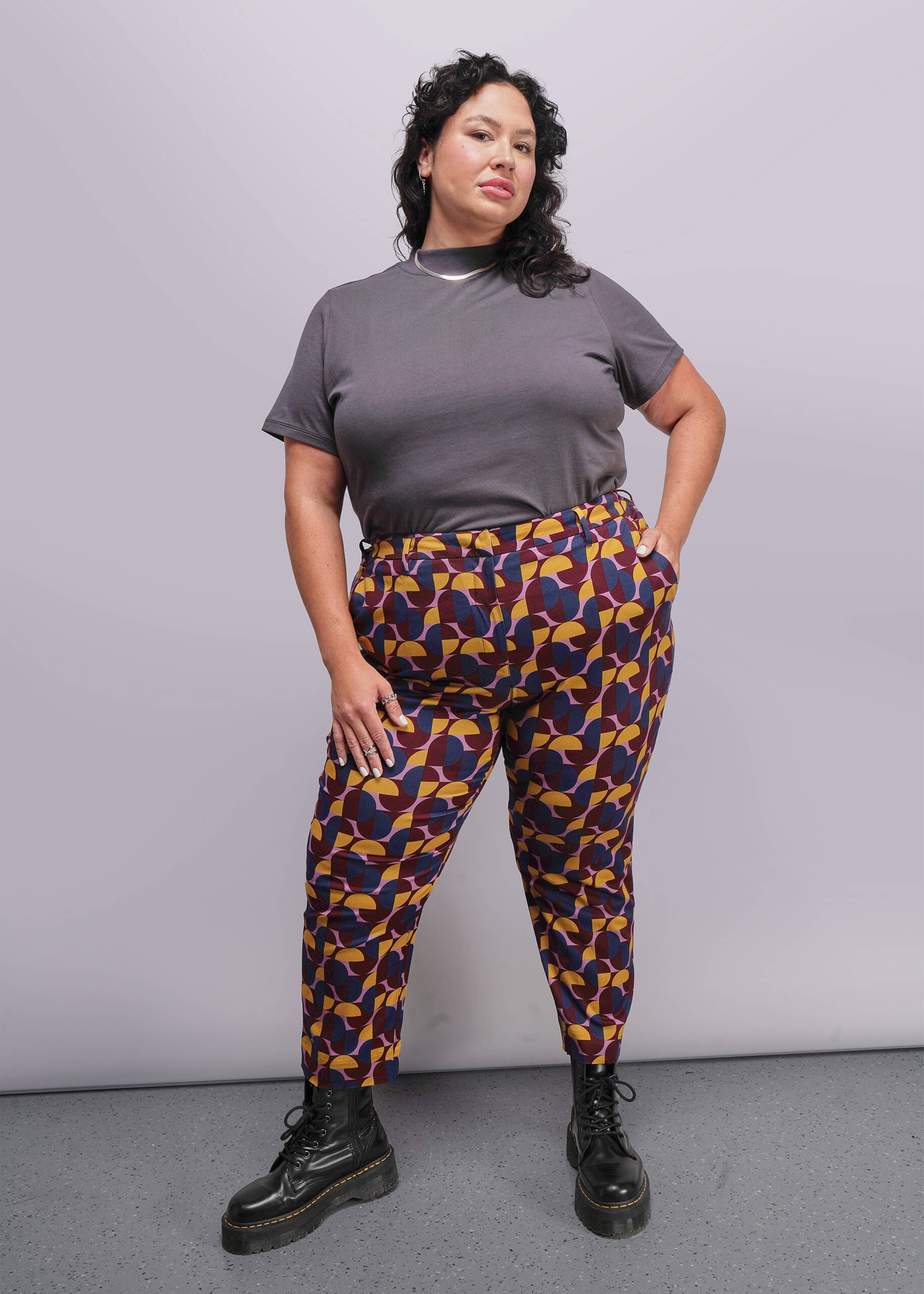 S=Woman wearing a gray t-shirt and colorful patterned pants against a plain background