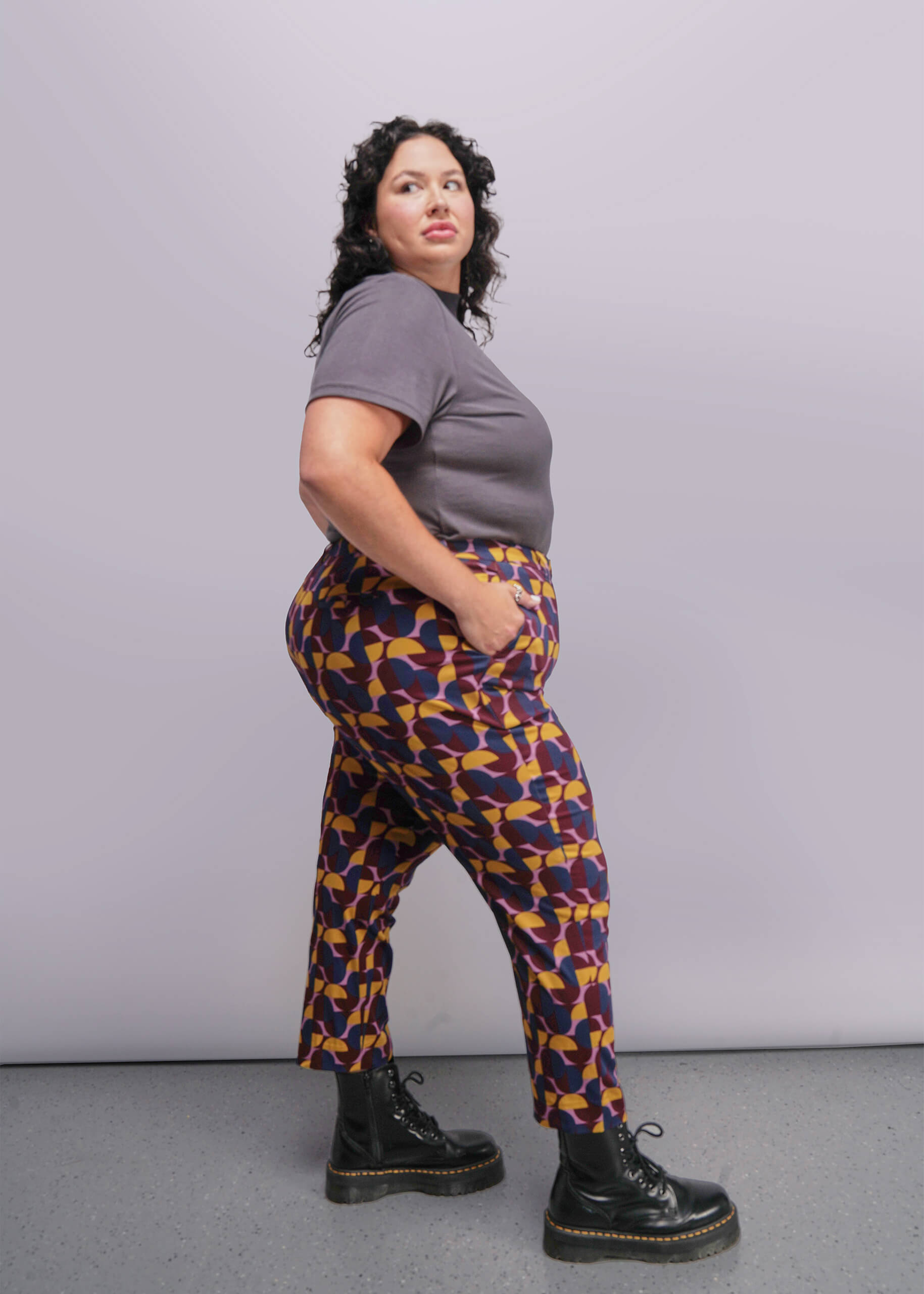 S=Person wearing a gray shirt and patterned pants against a plain background