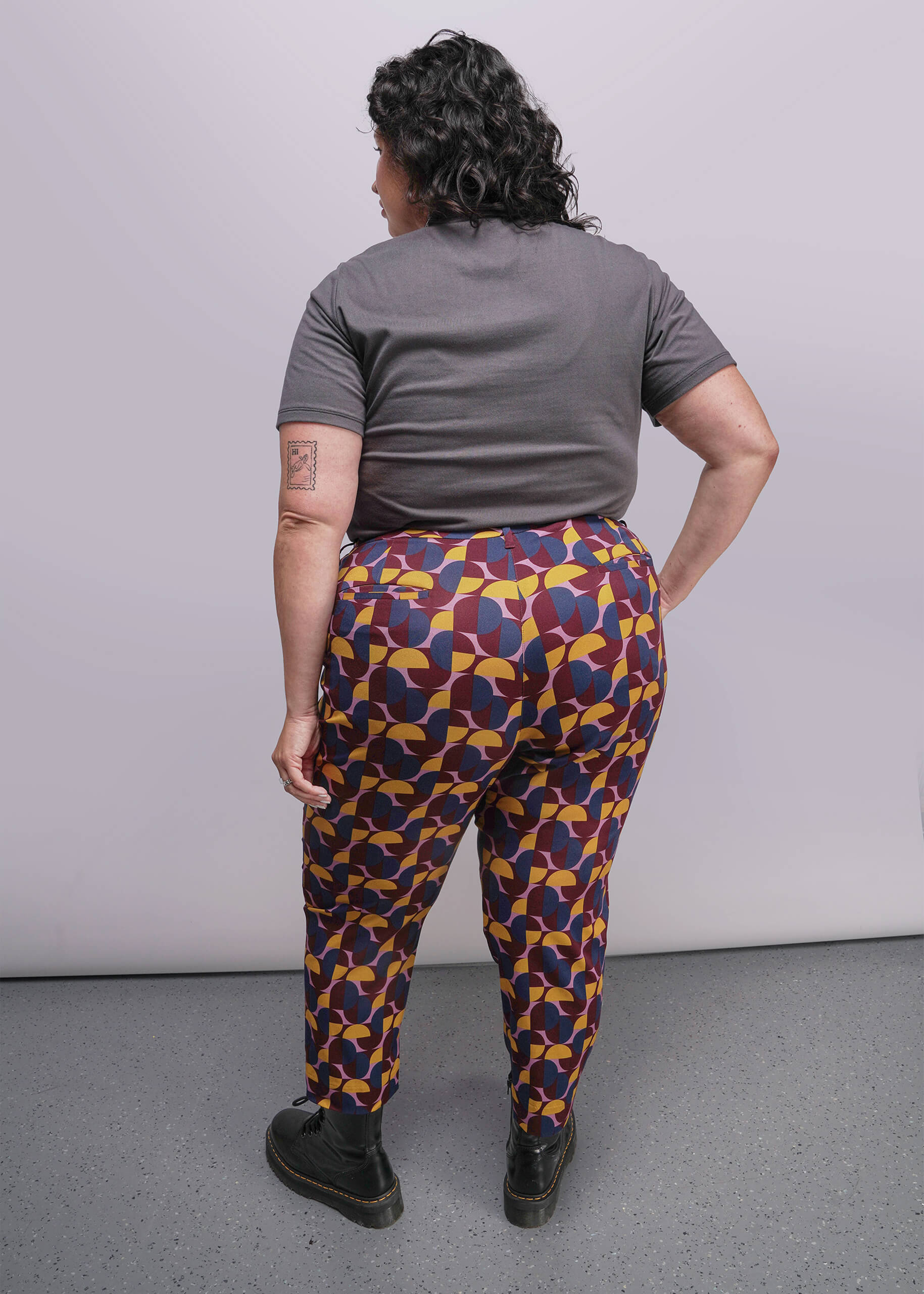 S=Person wearing colorful patterned pants and a gray shirt against a plain background