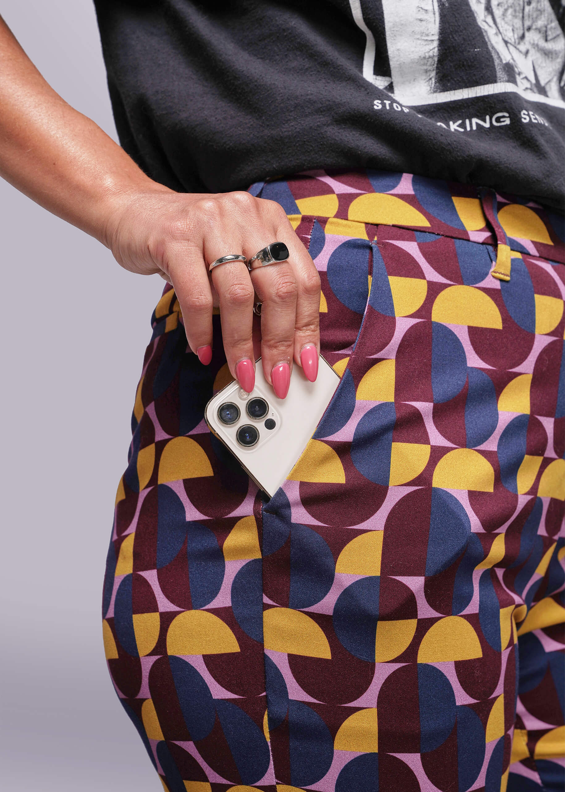 S=Person wearing a colorful geometric-patterned skirt holding a phone with a gray background