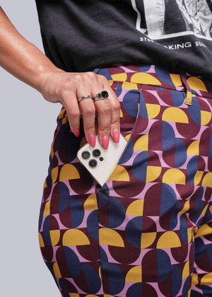 S=Person wearing a colorful geometric-patterned skirt holding a phone with a gray background